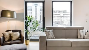 Una sala moderna con un sofá, una silla, una lámpara de pie y una planta en maceta.