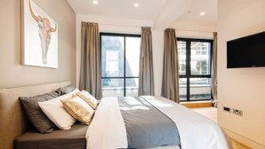 Un dormitorio moderno con una cama grande, un televisor de pantalla plana y vistas a la ciudad desde las ventanas.