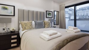 Een moderne hotelkamer met een groot bed, een nachtkastje, een spiegel en uitzicht op de stad door grote ramen.