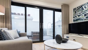 Een moderne woonkamer met een bank, een ronde salontafel, een televisie en een groot raam met uitzicht op een gebouw en een reuzenrad.