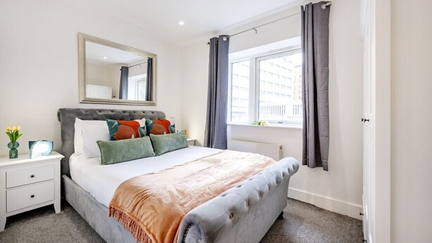 A bedroom with a large bed, a nightstand, a mirror, and a window with curtains. - Lovely 1 Bedroom at the British Museum (Greater London)