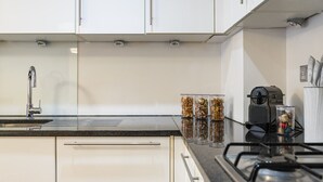 A modern kitchen with white cabinets, a stainless steel sink, a gas stove, and a coffee maker. - Lovely 1 Bedroom at the British Museum (Greater London)
