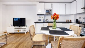 A modern kitchen with white cabinets, a microwave, and a dining area with a table and chairs. - Lovely 1 Bedroom at the British Museum (Greater London)