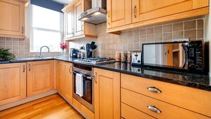 A modern kitchen with wooden cabinets, a stainless steel range hood, a microwave, and a coffee maker. - Elegant 1 Bedroom in Cambridge Circus (Greater London)