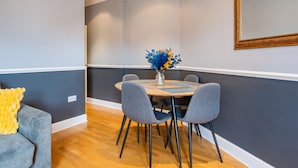 A dining area with a round table, grey upholstered chairs, and a vase with flowers. - Elegant 1 Bedroom in Cambridge Circus (Greater London)