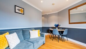 A modern living room with a grey sofa, a dining table with chairs, a large mirror, and a framed artwork on the wall. - Elegant 1 Bedroom in Cambridge Circus (Greater London)