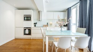 A modern kitchen with white cabinetry, a glass dining table, and a vase of flowers. - Splendid 2 Bedroom in Covent Garden (Greater London)