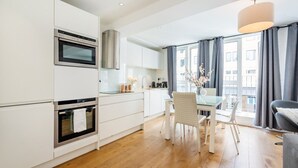 A modern kitchen with white cabinetry, stainless steel appliances, and a dining area with a glass table and chairs. - Splendid 2 Bedroom in Covent Garden (Greater London)