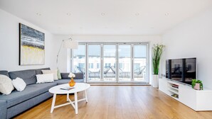 Una sala de estar moderna con un sofá gris, una mesa de centro blanca y un televisor grande sobre un mueble blanco.