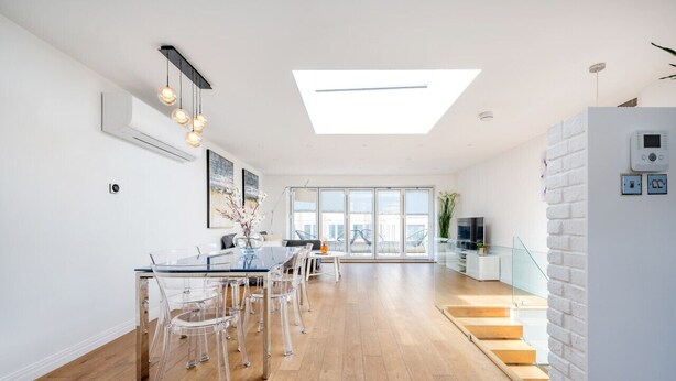 Un espacio habitable moderno con comedor, una escalera y un gran ventanal que proporciona luz natural.