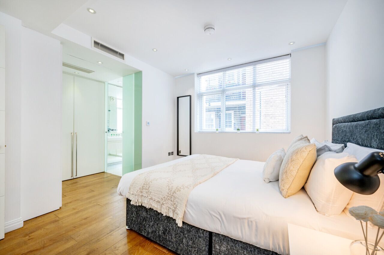 Une chambre à coucher moderne avec un grand lit, une fenêtre avec des stores et une porte donnant sur une autre pièce.