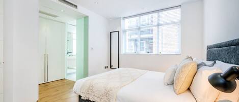 Une chambre à coucher moderne avec un grand lit, une fenêtre avec des stores et une porte donnant sur une autre pièce.