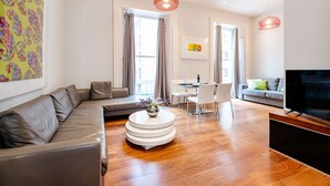 Una sala de estar moderna con un sofá gris, una mesa redonda de centro, un televisor y un comedor con una mesa y sillas.