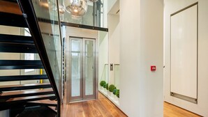 Un interior moderno con suelo de madera, un ascensor de cristal y una puerta blanca.