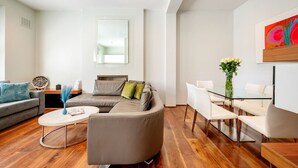 Ein modernes Wohnzimmer mit einer Eckcouch, einem Glastisch und einem Essbereich mit weißen Stühlen.