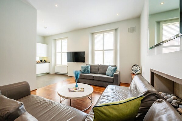 A modern living room with a grey sofa, a round coffee table, and a TV. - Chic 2 Bedroom Retreat in South Kensington (Greater London)