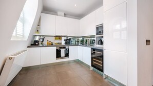 A modern kitchen with white cabinetry, a built-in oven, and a window providing natural light. - Chic 2 Bedroom in South Kensington (Greater London)
