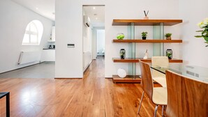 A modern kitchen with wooden shelves, a glass dining table, and a view through an open doorway. - Chic 2 Bedroom in South Kensington (Greater London)