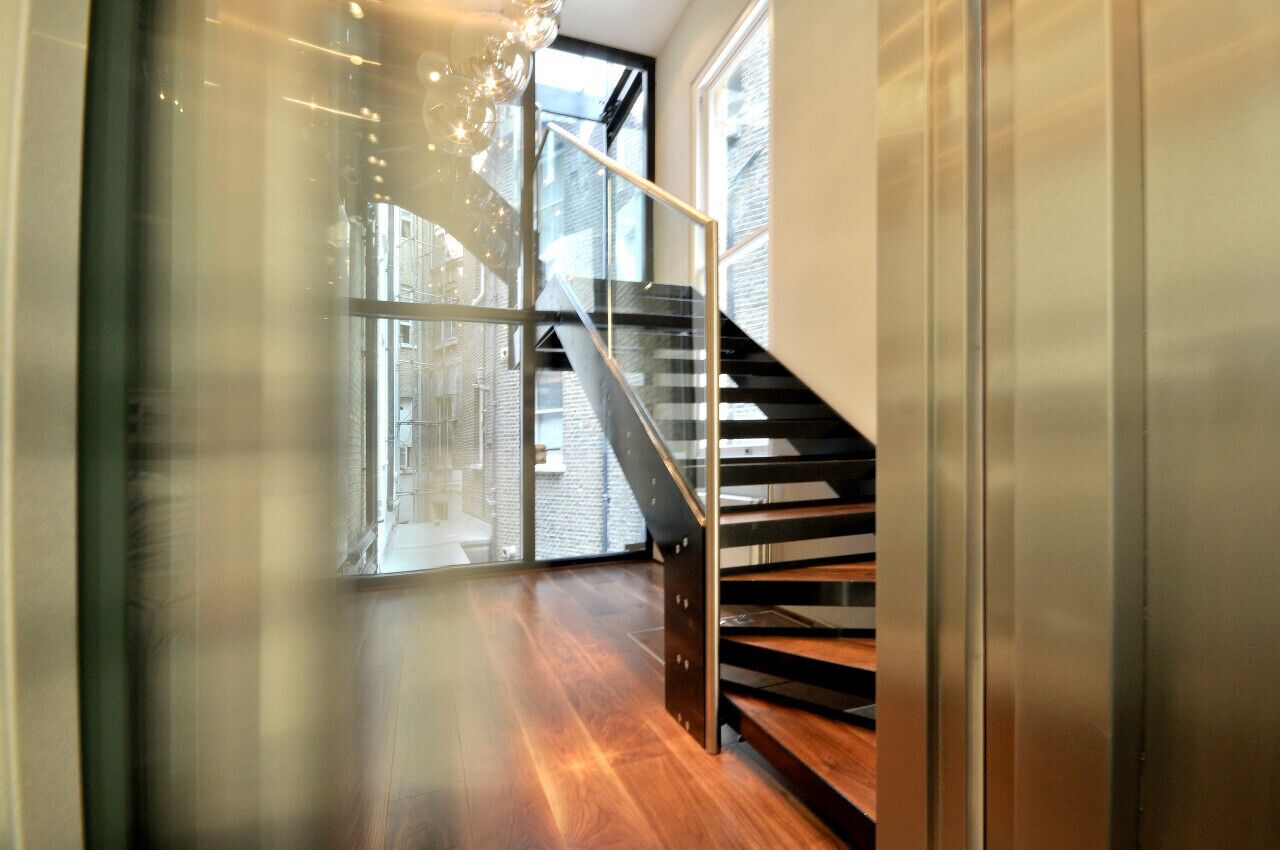 A modern interior with a wooden floor, a glass door, and a staircase with metal railings.