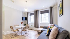 A modern living room with a grey sofa, a dining table with chairs, and a TV mounted on the wall. - Unique Covent Garden Townhouse! (Greater London)