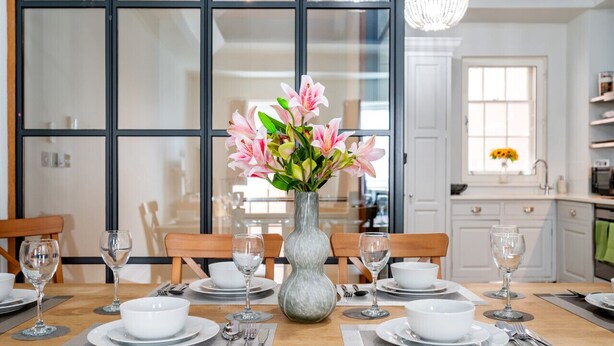 A dining table set for six with white plates, bowls, and wine glasses, centered by a vase of pink flowers. - Unique Covent Garden Townhouse! (Greater London)