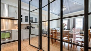 A modern kitchen with white cabinets and stainless steel appliances, a dining area with wooden furniture, and large windows allowing natural light. - Unique Covent Garden Townhouse! (Greater London)