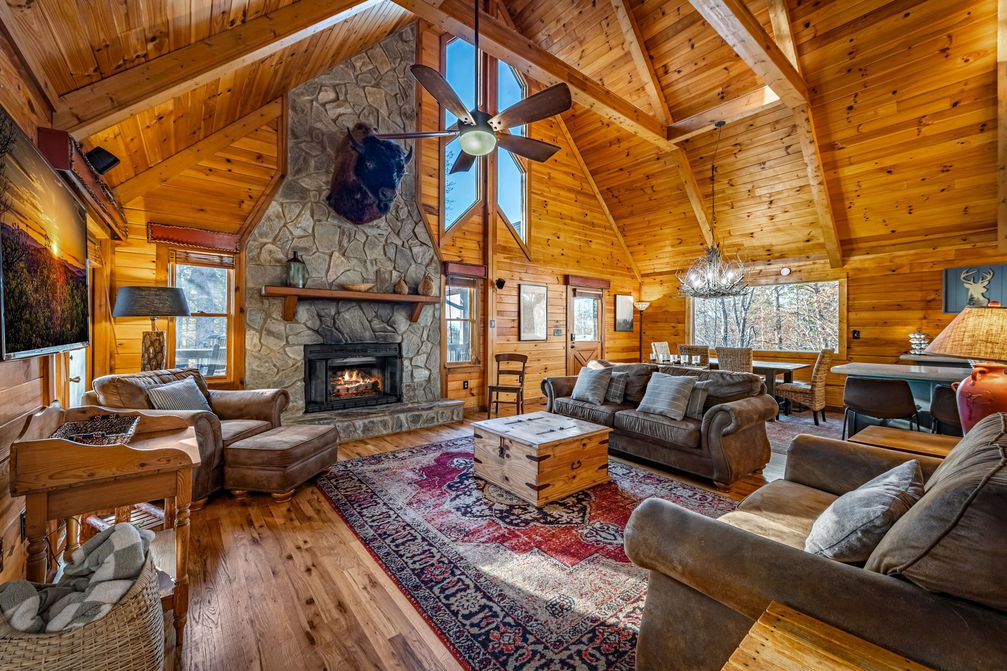 L’intérieur d’une cabane en rondins, avec une cheminée en pierre, des meubles en bois et un grand ventilateur de plafond.