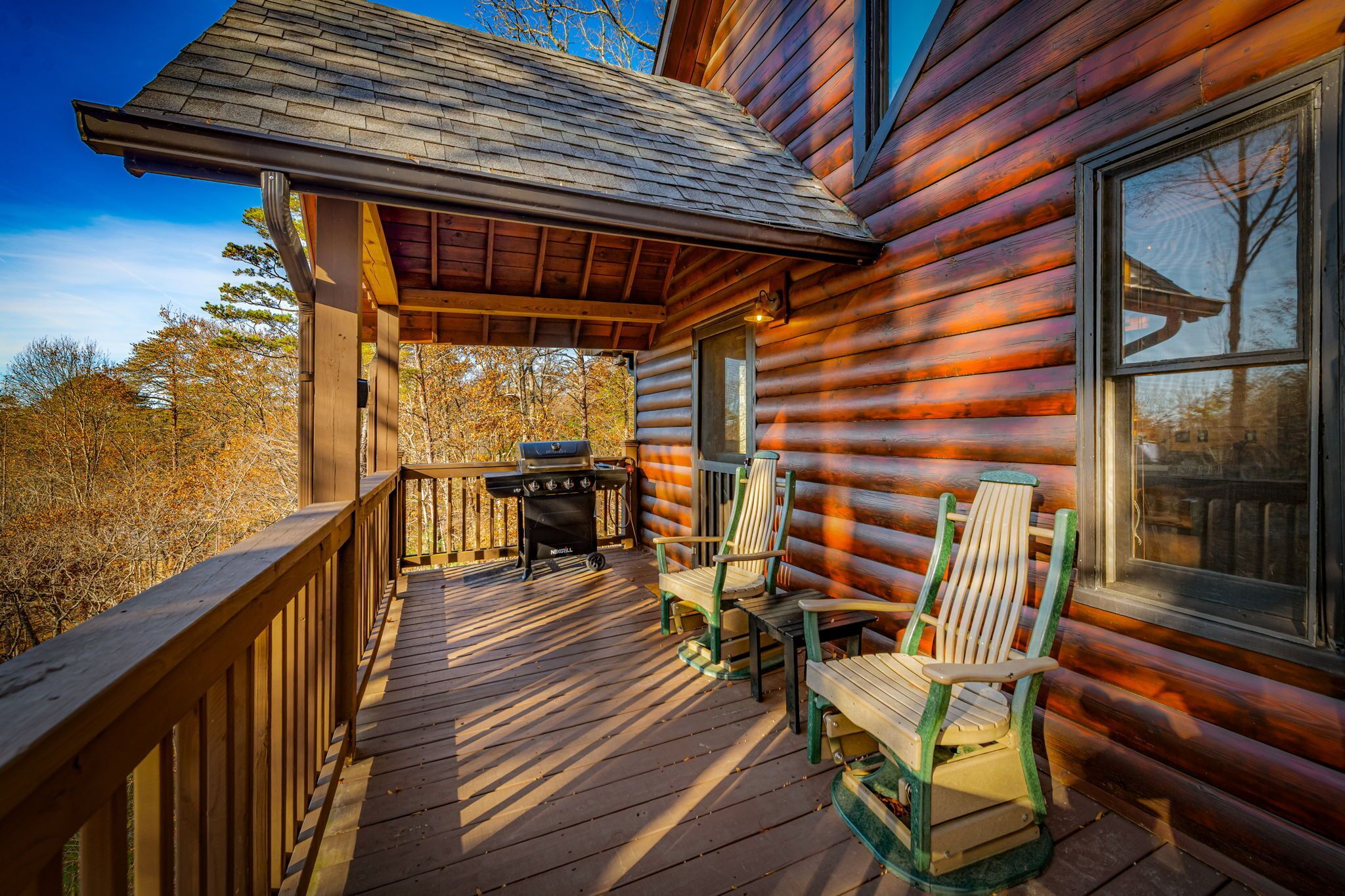 Eine Blockhütte mit Veranda, Grill und Adirondack-Stühlen.
