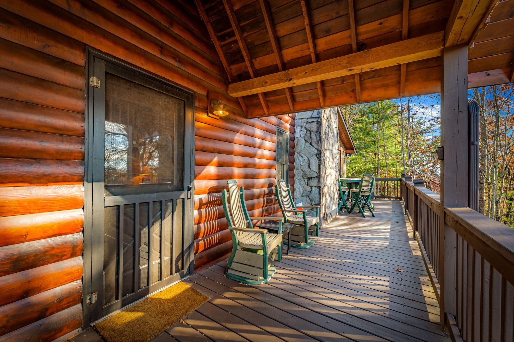 A log cabin with a wooden deck, outdoor seating, and a stone wall.
