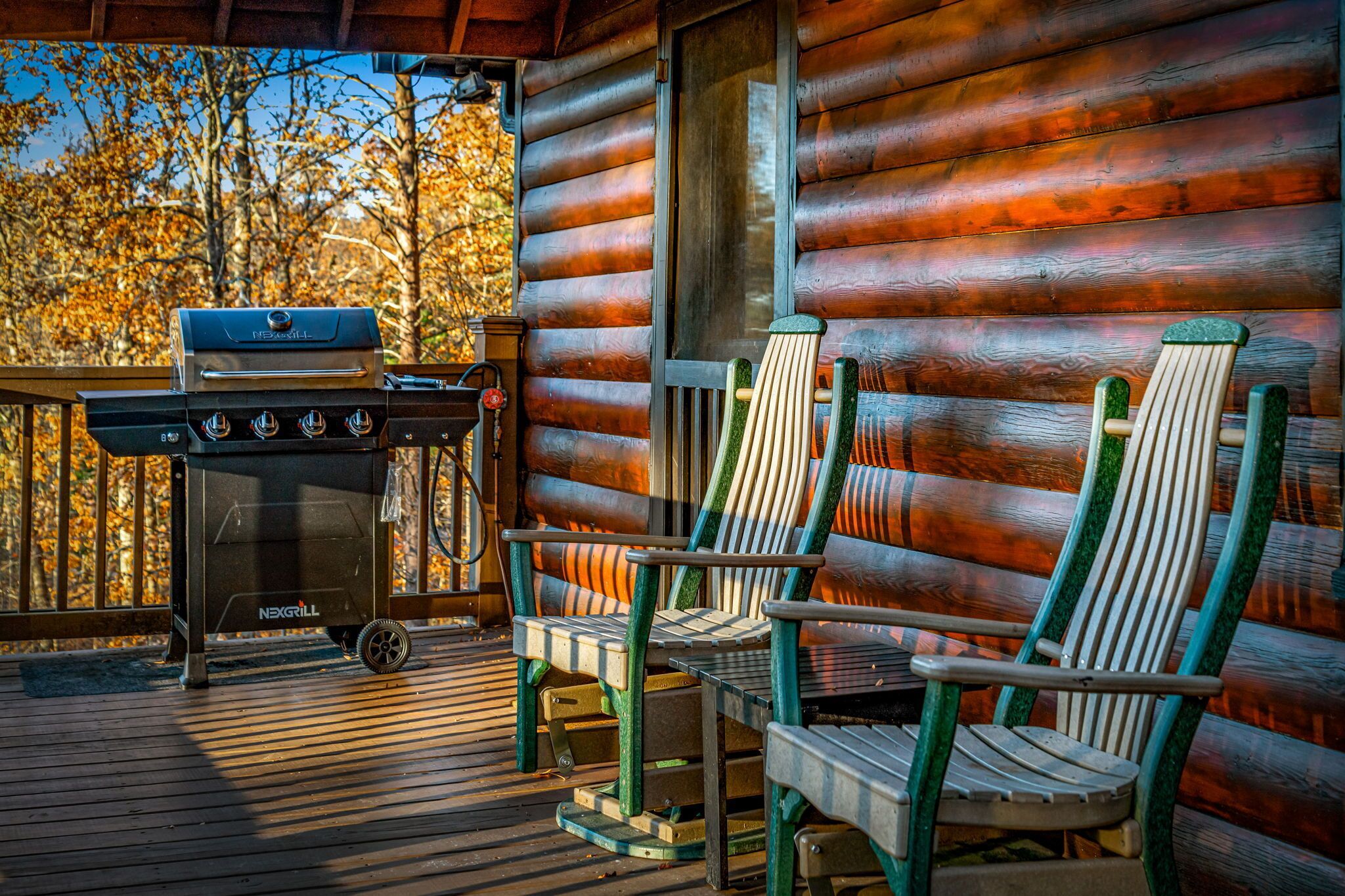 Una terraza de madera con una parrilla y sillas Adirondack.