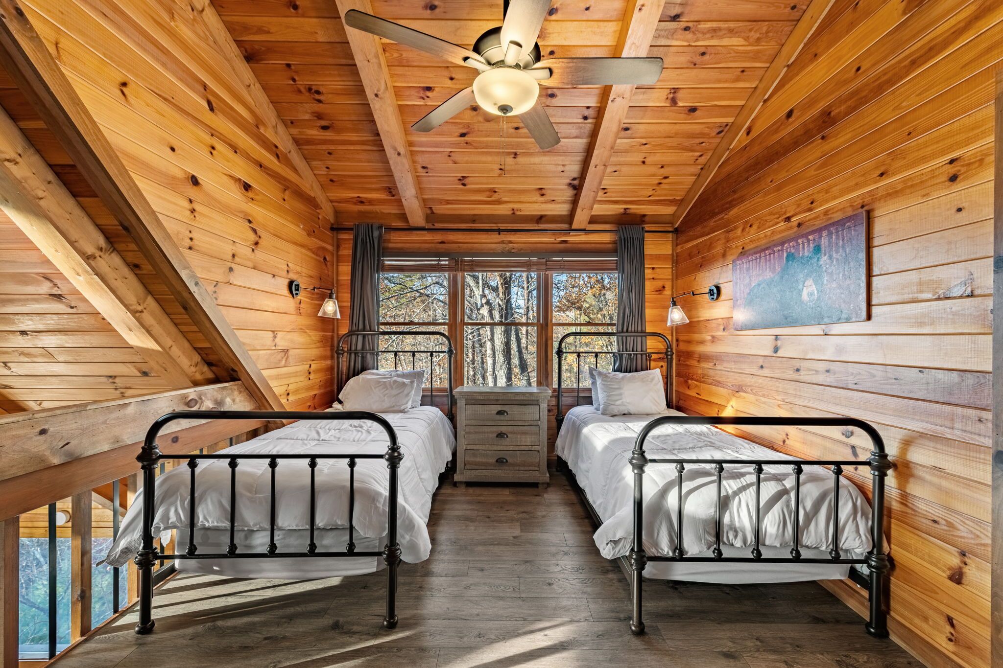 A cabin with two metal beds, a ceiling fan, a dresser, and a large window.