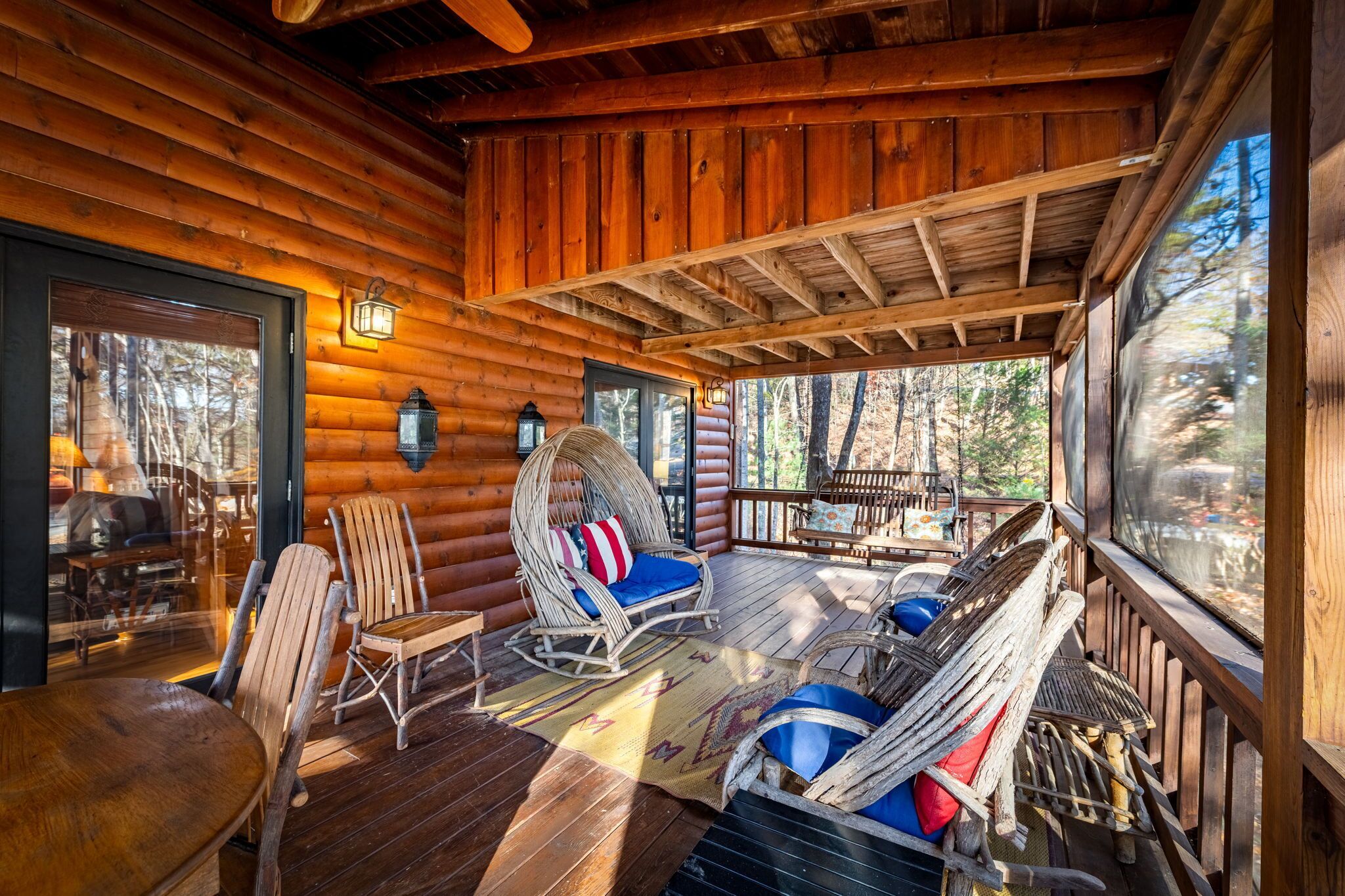 A log cabin with a porch, wicker chairs, a rocking chair, and a view of the forest.