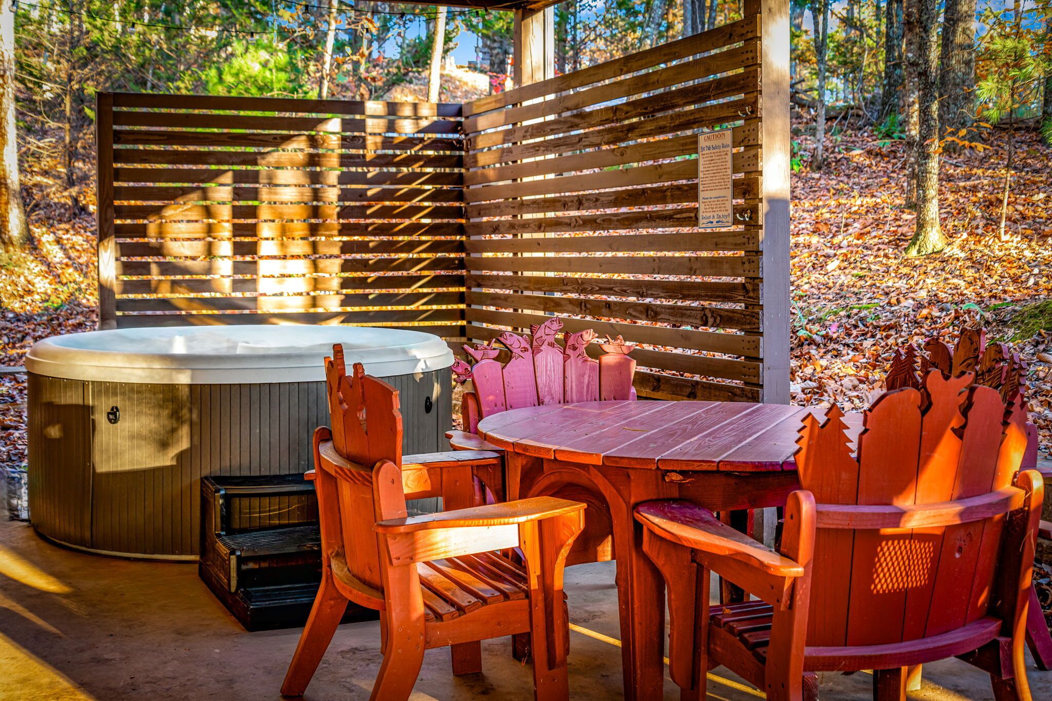 A wooden hot tub, a table, and chairs in a forested area.