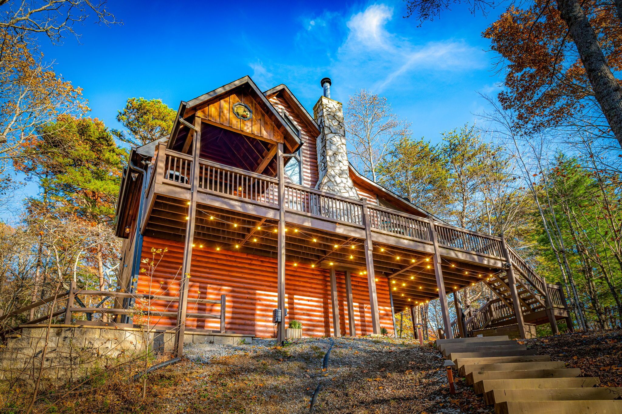 A log cabin with a balcony, a stone chimney, and a staircase leading up to the entrance.