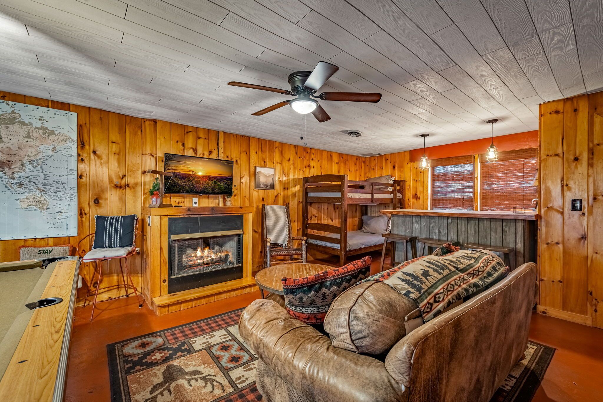 A cozy cabin interior with a wooden interior, a fireplace, a sofa, a pool table, and a bar area.