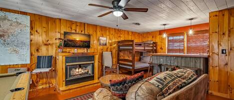 A cozy cabin interior with a wooden interior, a fireplace, a sofa, a pool table, and a bar area.