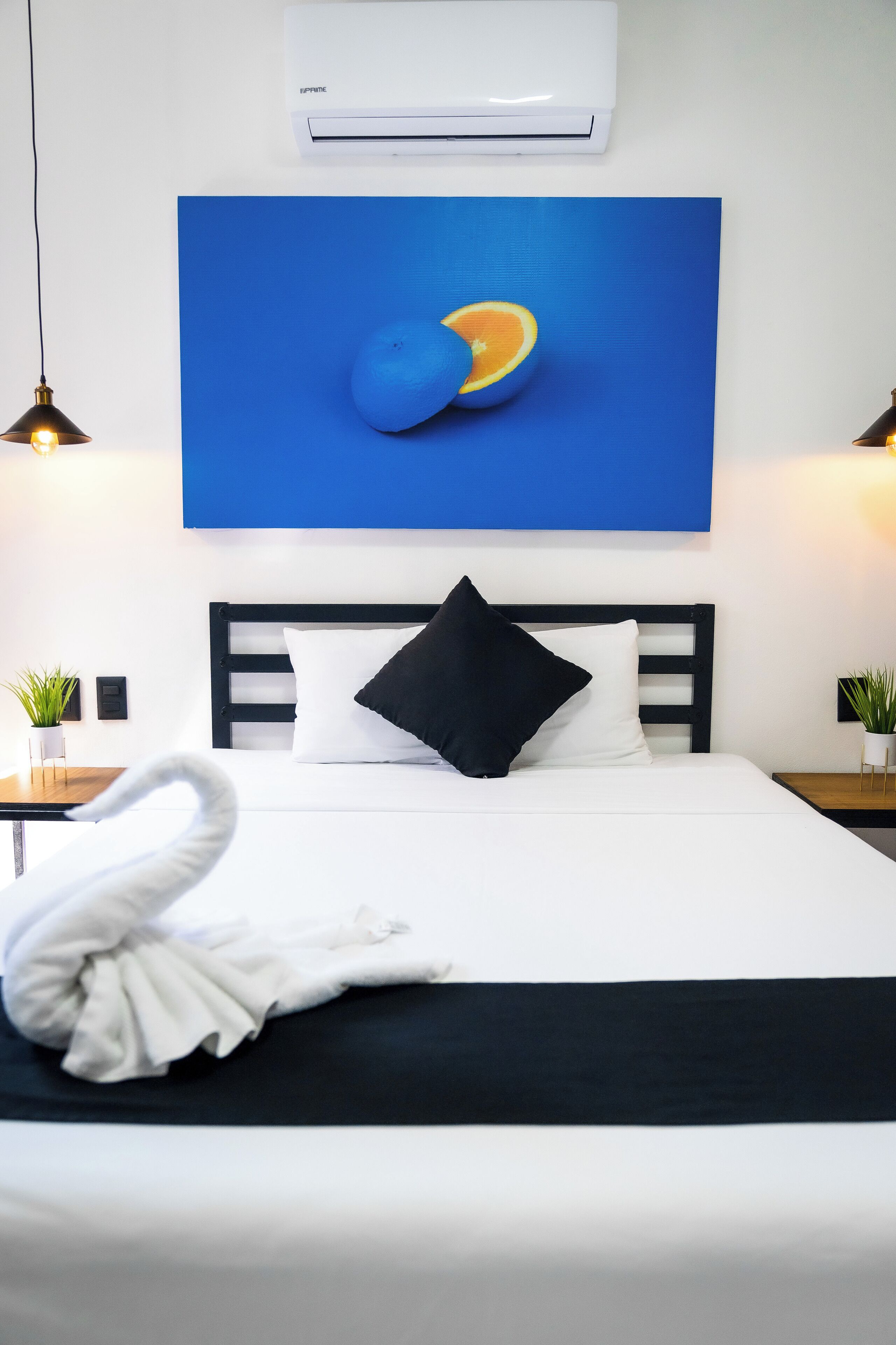 Ein Hotelzimmer mit einem Bett, einer Wandklimaanlage, einem blauen Gemälde und zwei Nachttischlampen.