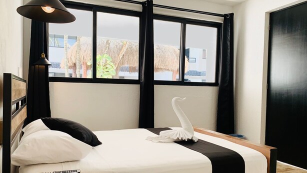 Una habitación de hotel moderna con una cama grande, una mesita de noche, una lámpara y vistas al exterior.
