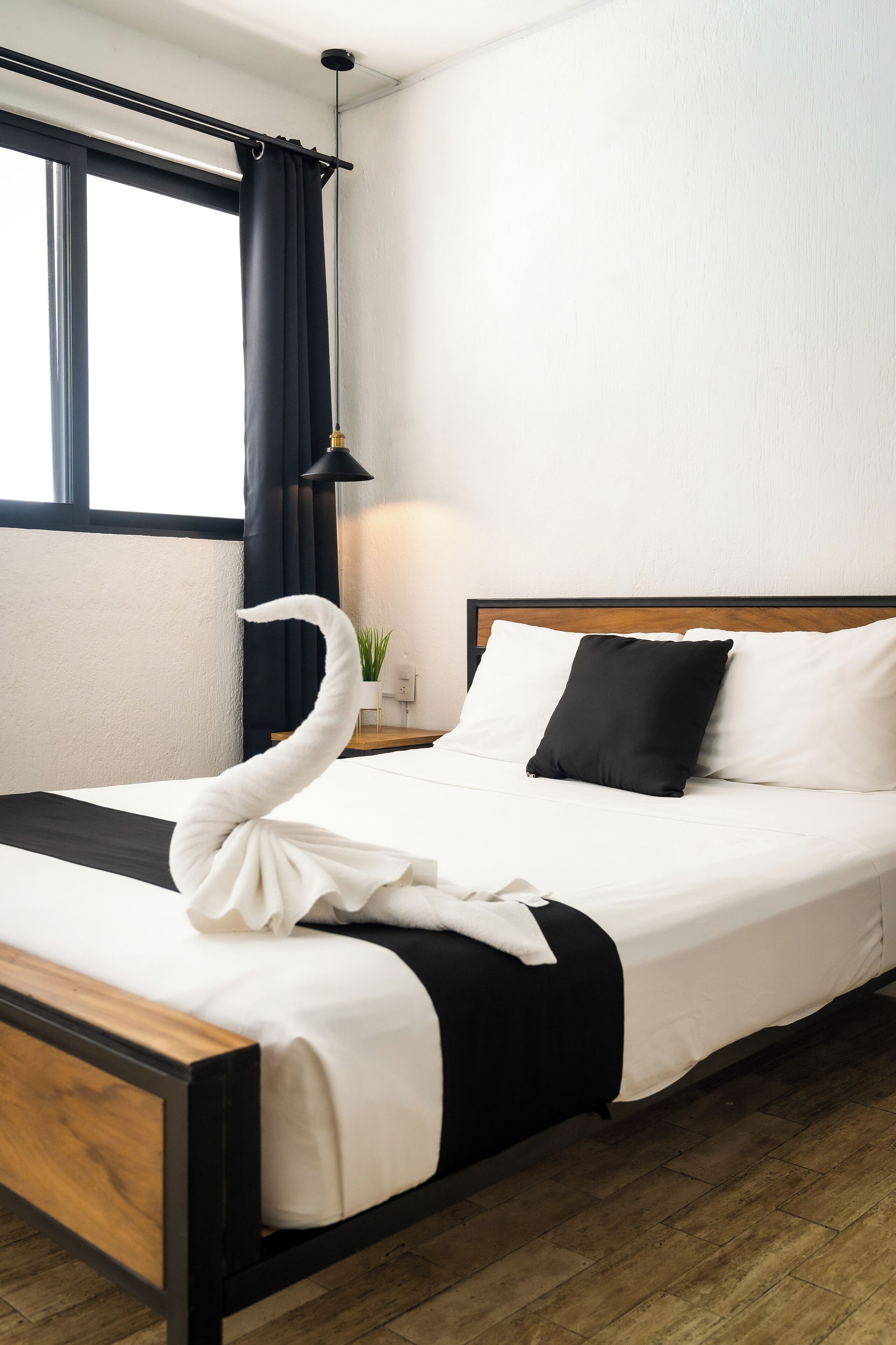 A neatly made bed with a black and white pillow set, a wooden headboard, and a swan-shaped towel.