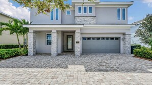 A modern two-story house with a stone facade, a garage, and a paved driveway. - 8BR Spectacular Villa • Games Room • Near Disney (Kissimmee)