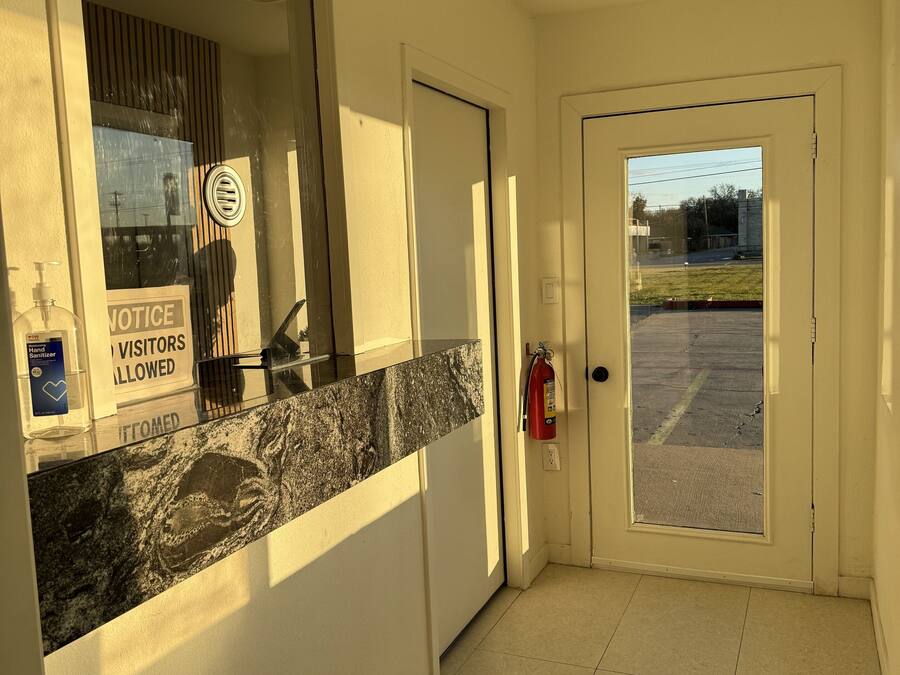 A reception area with a marble counter, a notice for visitors, a fire extinguisher, and a view of the parking lot.