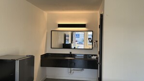 Une petite salle de bain avec un lavabo noir encastré dans le comptoir, un miroir au-dessus et une tuyauterie visible en dessous.
