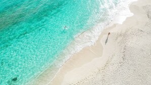 Luchtbeeld van een strand met helder turquoise water en een zandstrand.