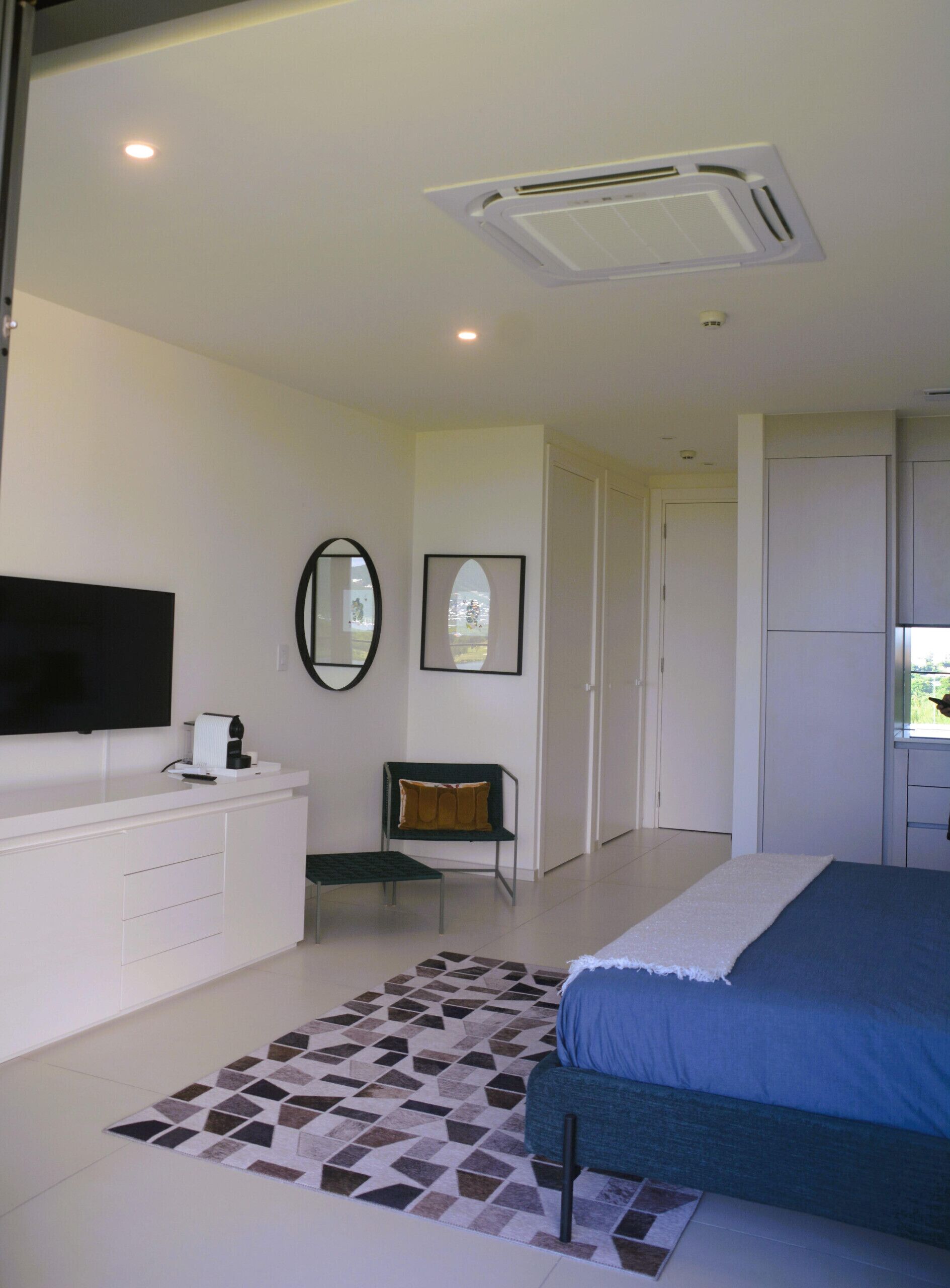 A bedroom with a bed, a TV, a desk, a chair, and a window.