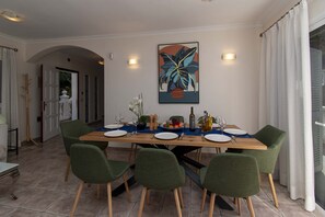 A dining area with a wooden table set for four, green chairs, and a large abstract painting on the wall. - Villa Catherine (Costa Adeje)
