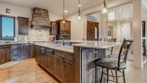 A spacious kitchen with a large island, dark wooden cabinets, and a stone accent wall. - Highland Heights! Luxe Mountain VIEWS w/ Hot Tub (Colorado Springs)