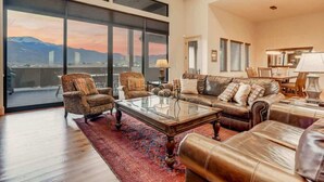A spacious living room with a large glass door leading to a balcony, leather furniture, and a city view. - Highland Heights! Luxe Mountain VIEWS w/ Hot Tub (Colorado Springs)