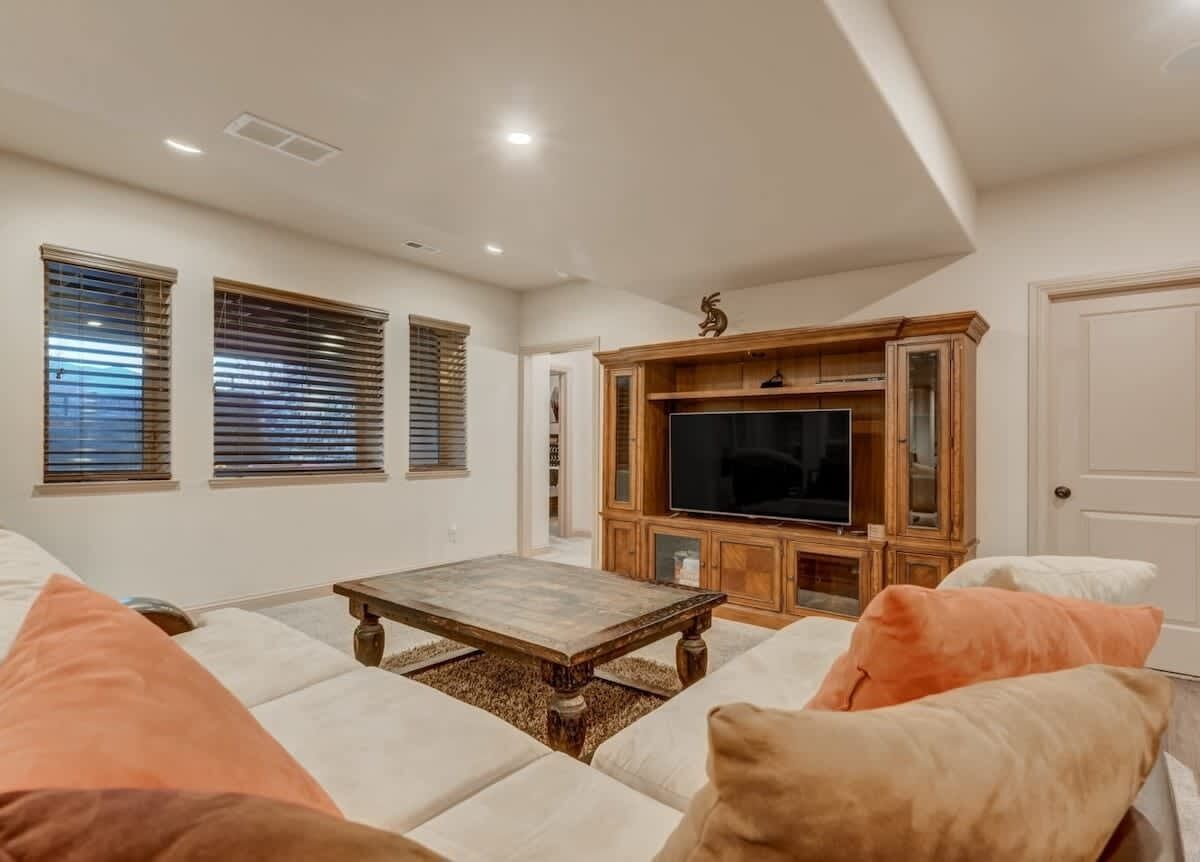 A living room with a large flat-screen TV, a wooden entertainment center, and a cozy seating area with cushions.