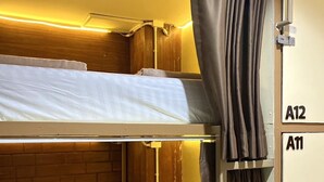 A bunk bed room with a wooden headboard, a curtain, and a wall-mounted cabinet with labels A12 and A11. - Long Doo Hostel (Ko Phi Phi)