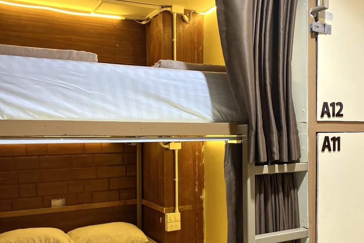 A bunk bed room with a wooden headboard, a curtain, and a wall-mounted cabinet with labels A12 and A11.